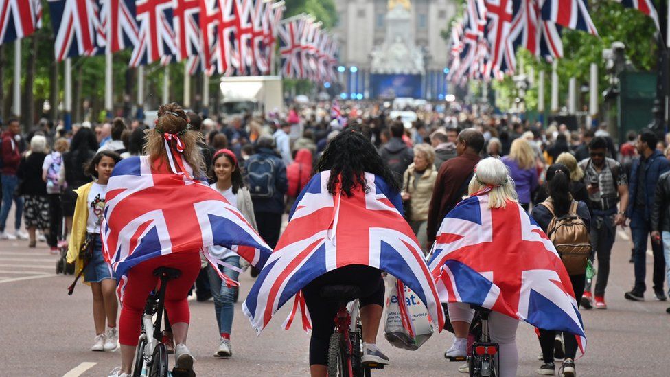 Women wearing Union Jack flags as capes, cycle down the mall towards Buckingham Palace
