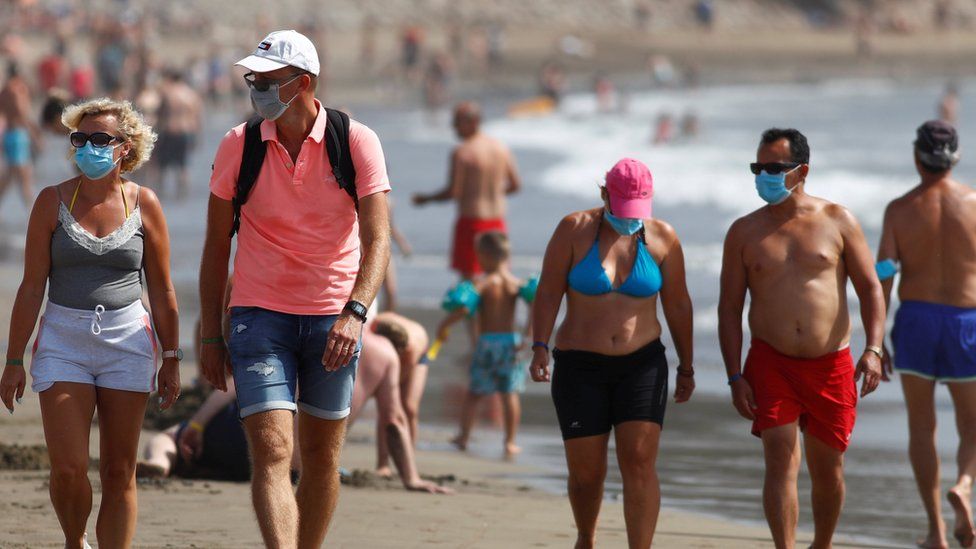 Several people walk along the beach wearing face masks in Playa del Ingles, Gran Canaria, Spain, August 14, 2020.