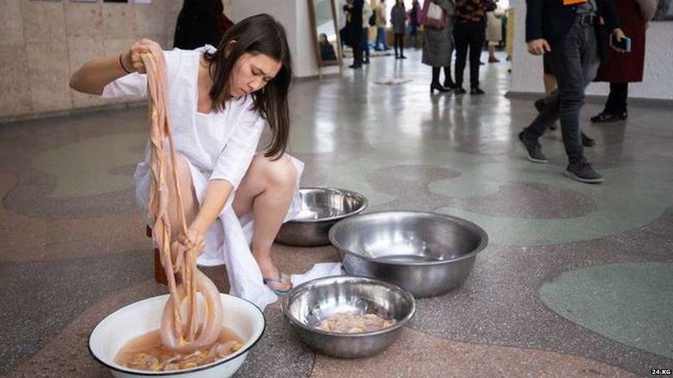 A young woman washing lamb intestines in a basin