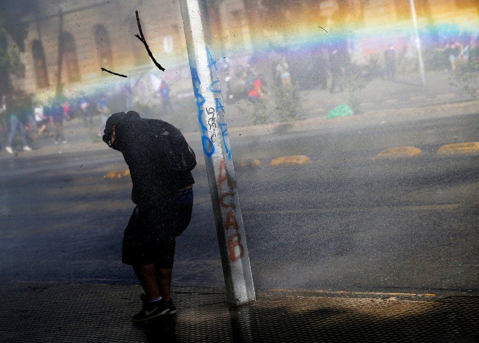 A demonstrator takes cover from tear gas and a water cannon during an anti-government protest in Santiago, Chile.