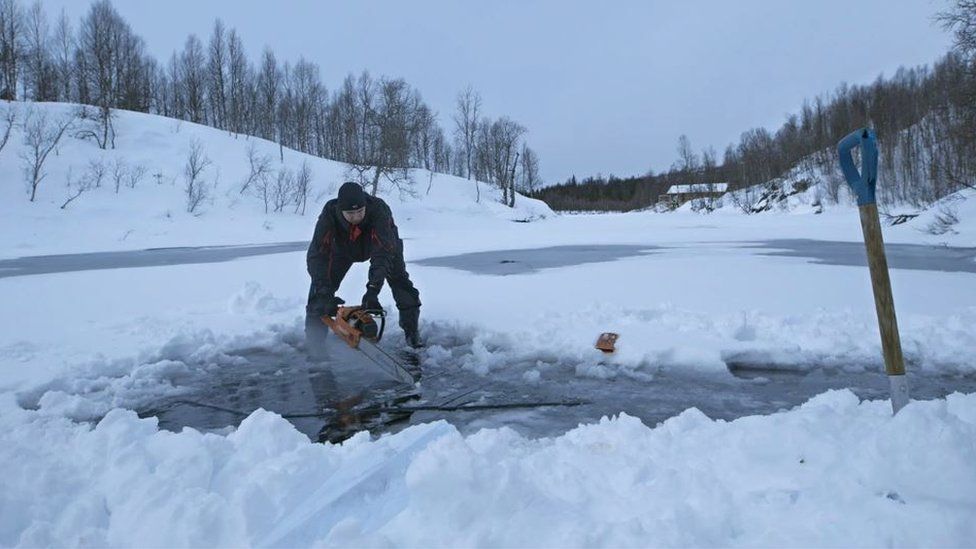 A man with a chainsaw, cutting a hole in the ice at Plura