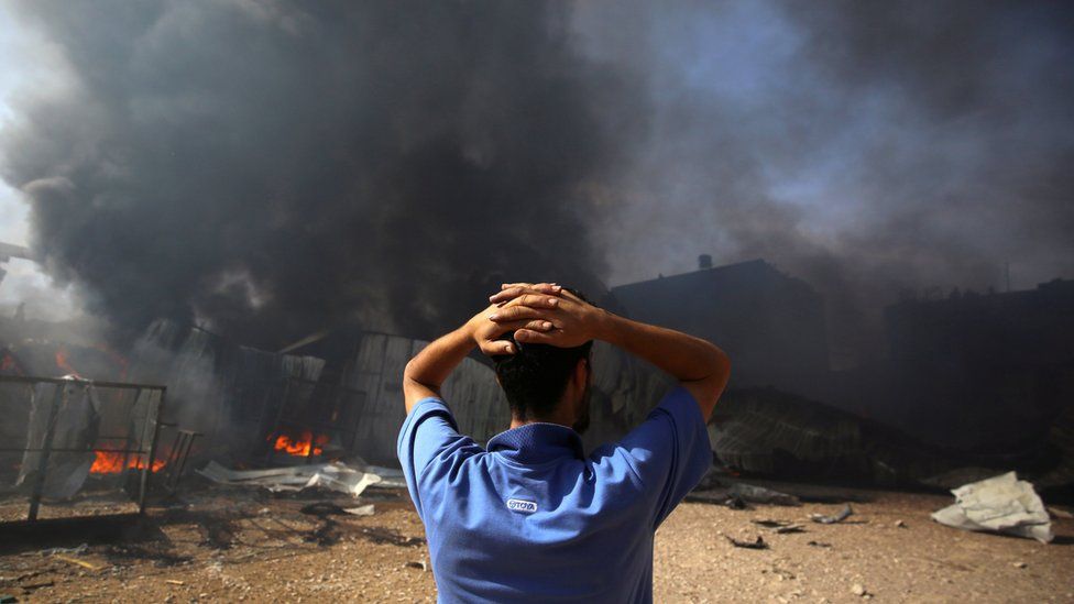 A man stands near a burning sponge factory after it was hit by Israeli artillery shells in Gaza