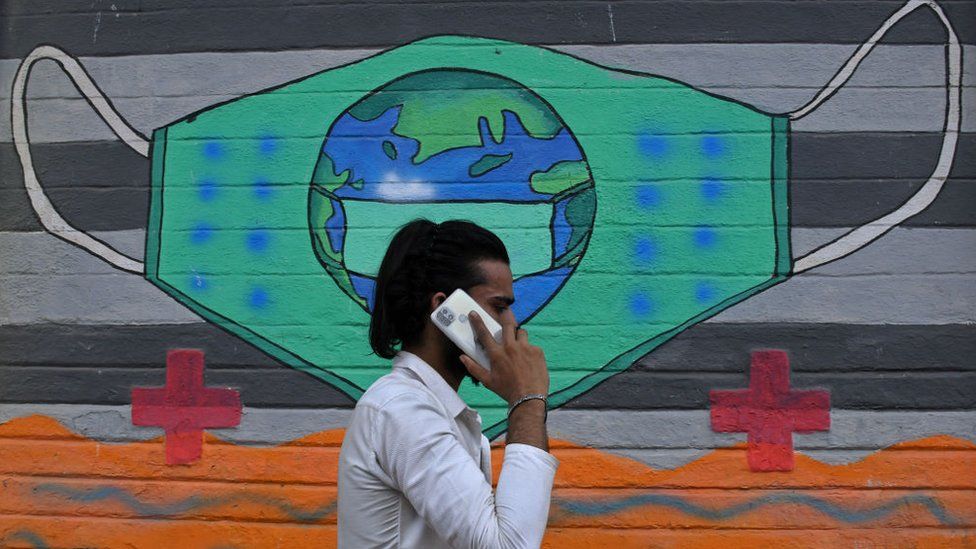 Мужчина, разговаривающий по телефону, проходит мимо граффити, нарисованного для повышения осведомленности о коронавирусной болезни в Мумбаи.