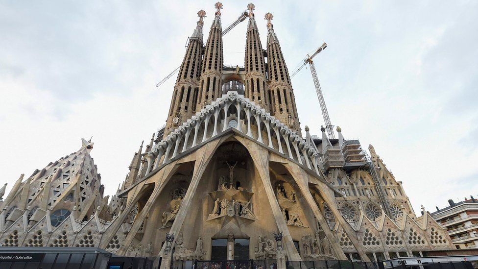 Tourists walk by the "Sagrada Familia" basilica in Barcelona