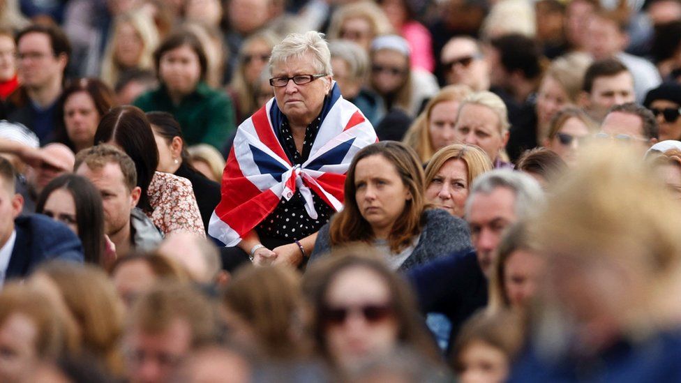 Woman with a Union Jack flag around her shoulders in a big crowd