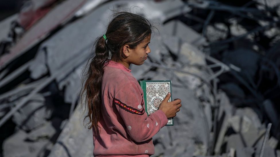 A young girl holds a copy of the Quran at the site of the destroyed Al Bokhari mosque following an Israeli airstrike in Deir Al Balah, southern Gaza Strip