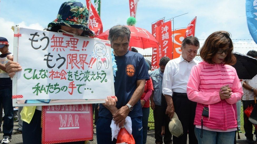 People offer a silent prayer in front of the US Kadena Air Base in Cyatan, Okinawa prefecture, 21 May