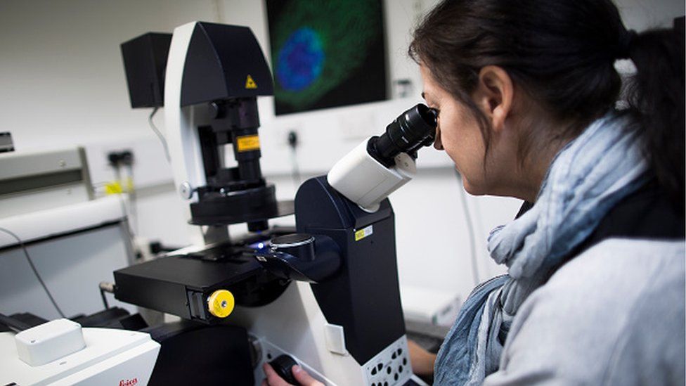 A woman looking through a microscope in a lab
