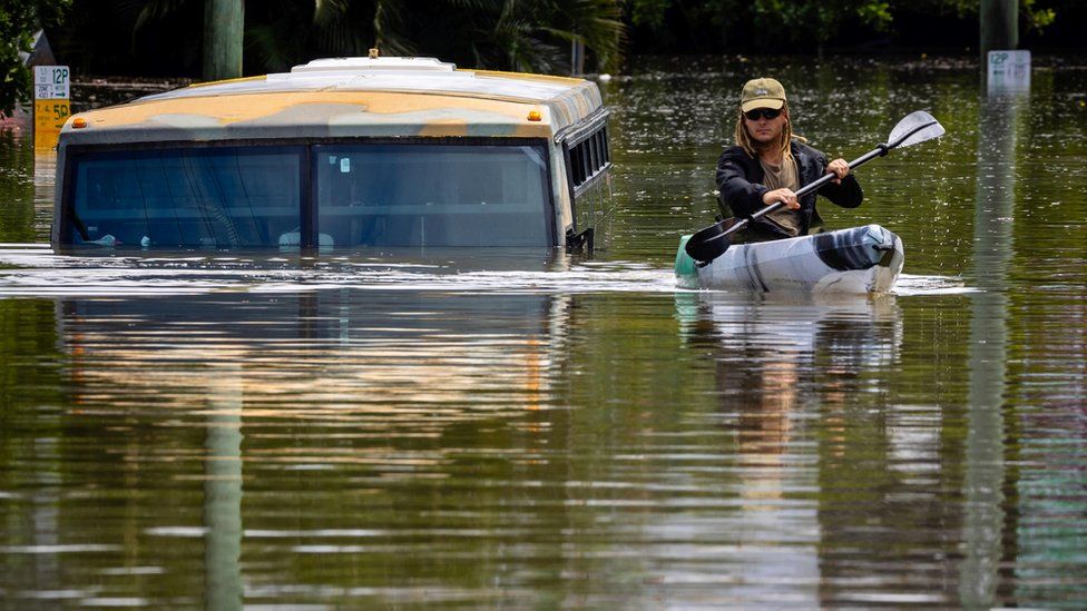 A man paddles his kayak next to a submerged bus on a flooded street in the town of Milton in suburban Brisbane on February 28, 2022.