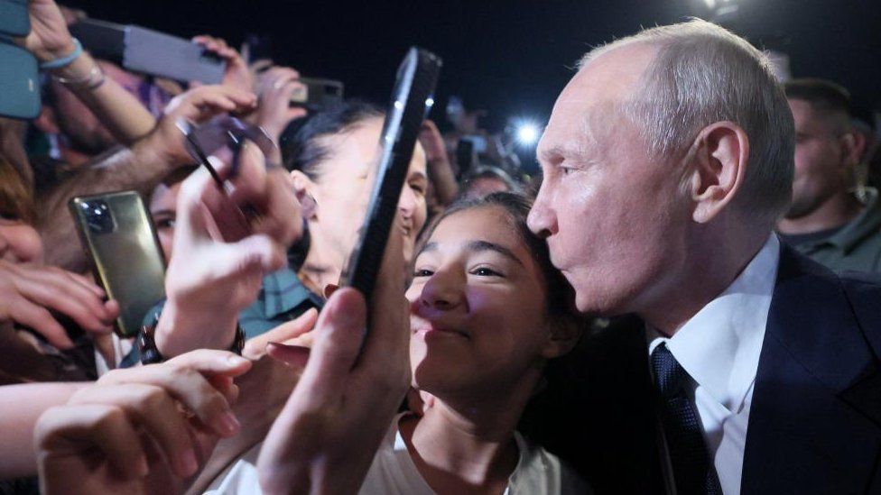 Il Presidente russo Vladimir Putin bacia la testa di una donna circondata da persone a Derbent, nella regione meridionale del Daghestan, in Russia, il 28 giugno 2023.