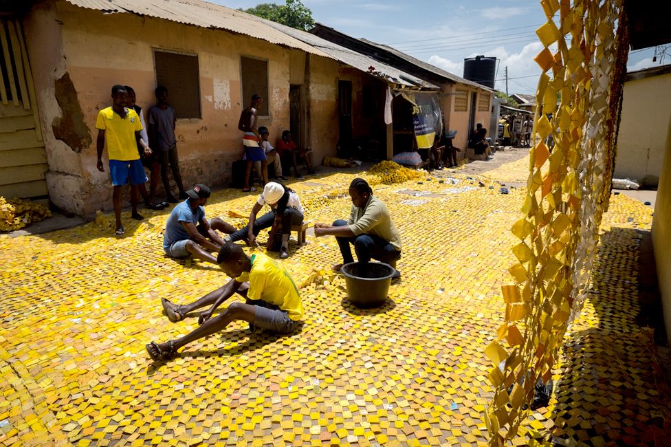 People sewing the yellow tapestry designed by artist Serge Attukwei Clottey on a road in La - Accra, Ghana