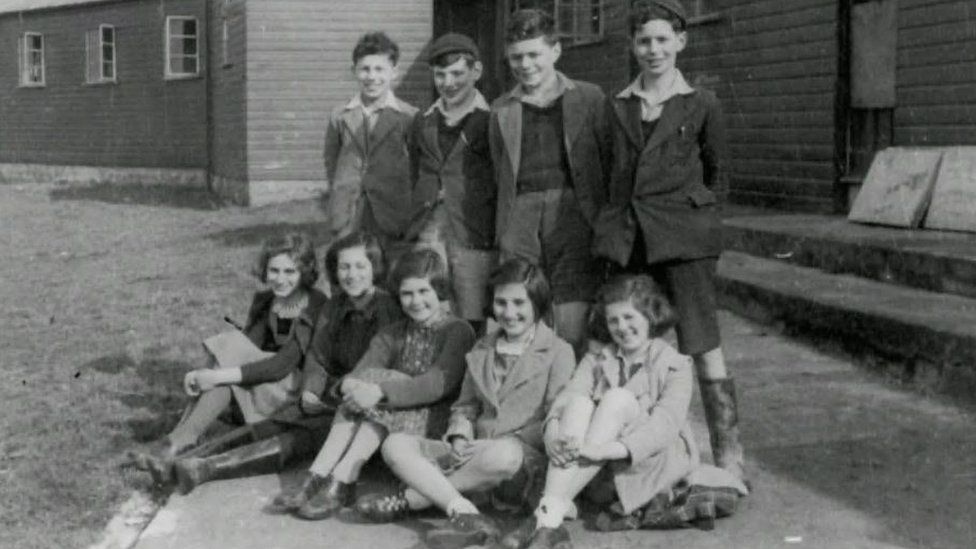 A group of young Jewish refugees pictured, with five girls sitting on the ground and four boys standing behind them