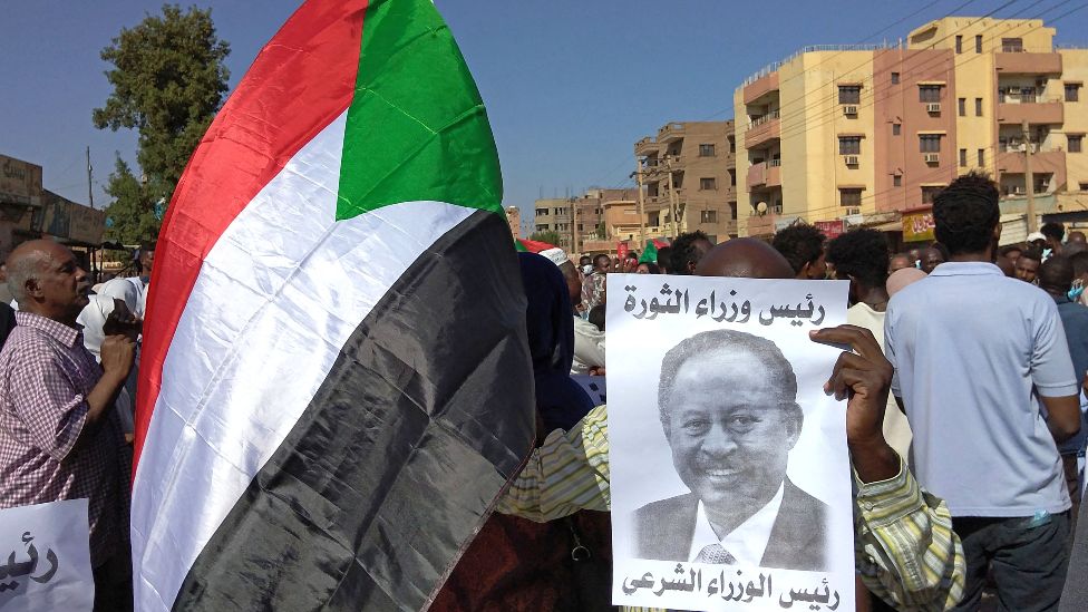 An anti-coup protester in Omdurman holds a placard showing ousted Sudanese Prime Minister Abdalla Hamdok, who is under house arrest, and reading: "Legitimate prime minister" - 17 November 2021