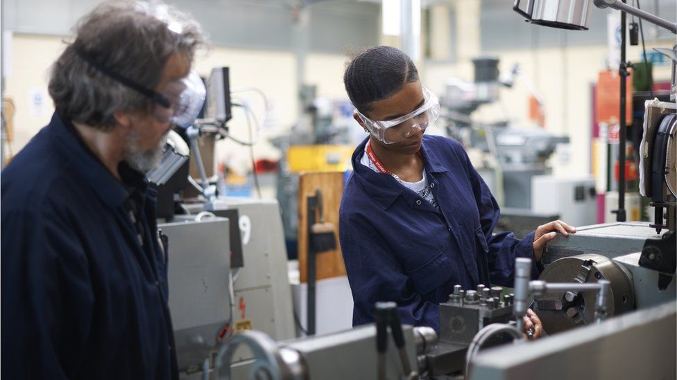 Generic image of an older man and young woman wearing overalls work in engineering roles