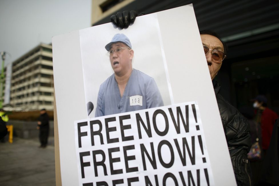 Man holding a placard with Kenneth Bae's photo and the words 'Free now'