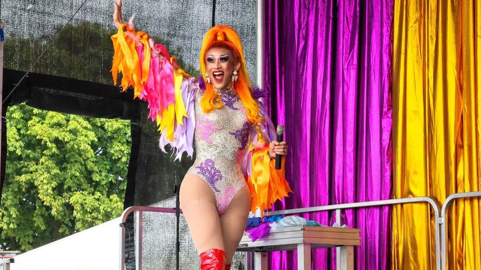 A performer in a brightly coloured outfit with tassels on the arms