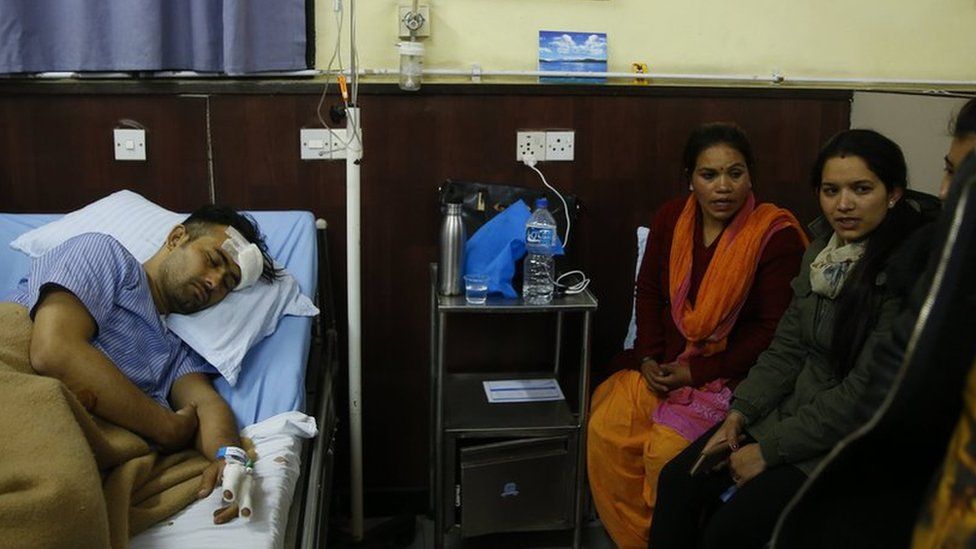 Basanta Bohora, who escaped the plane, sleeps in a hospital bed as family look on