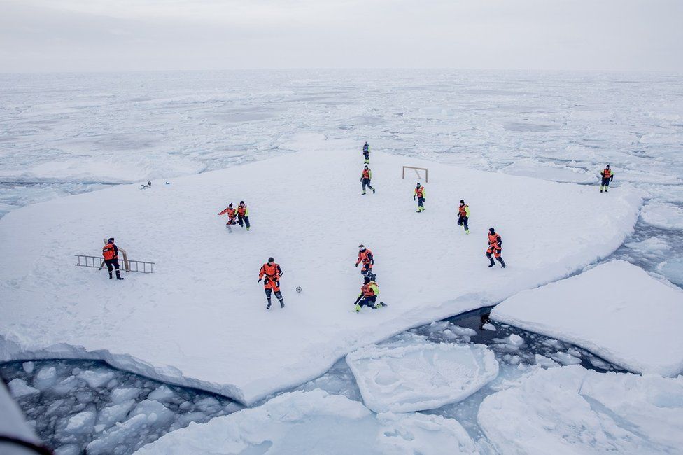 People play football on a large flat piece of ice in the sea