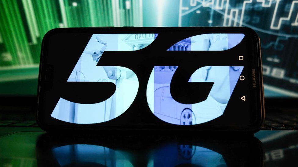 In this photo illustration a 5G logo is displayed on a smartphone with stock market percentages on the background.