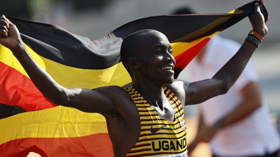 Man smiling holding Uganda flag above his head, 27 August