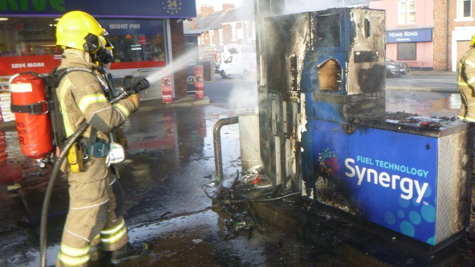 A firefighter hoses down a burnt petrol pump