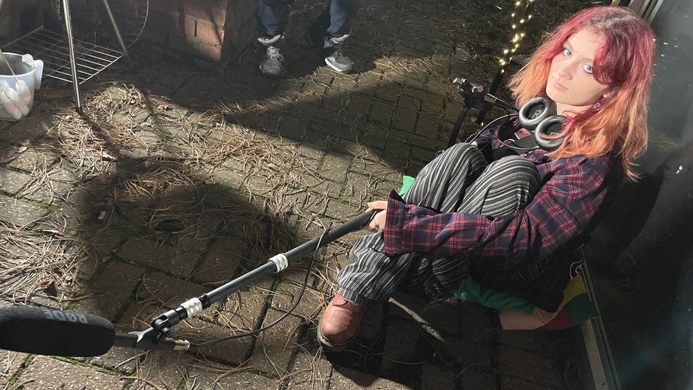 Red headed teenage girl holding a microphone on a boom stick.