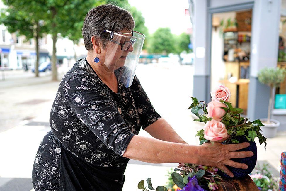 A woman puts out flowers on a stall whilst wearing a face shield