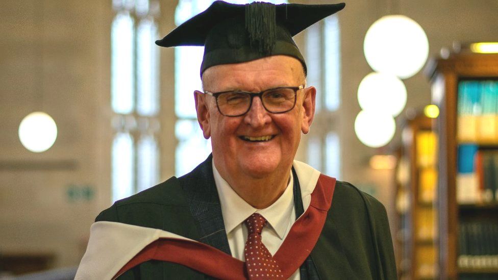 Paul Deal wearing his graduation robes and smiling at the camera