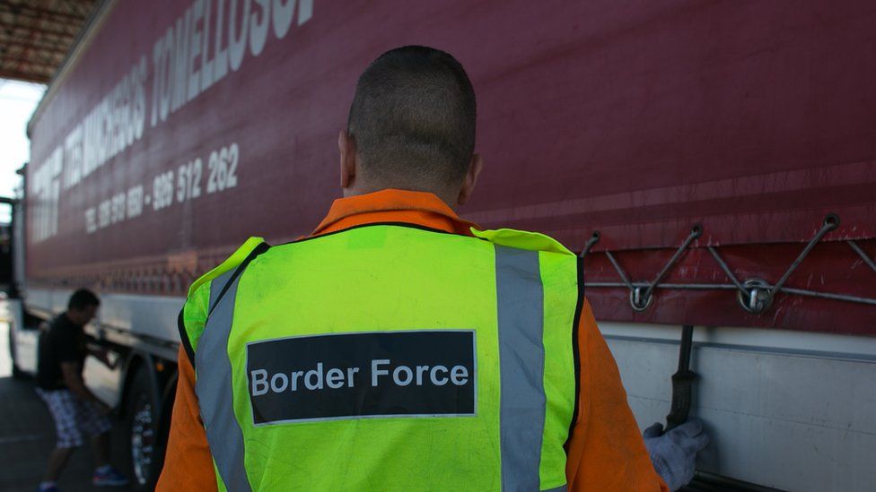 Man in high-vis jacket reading 'border force' inspects a lorry