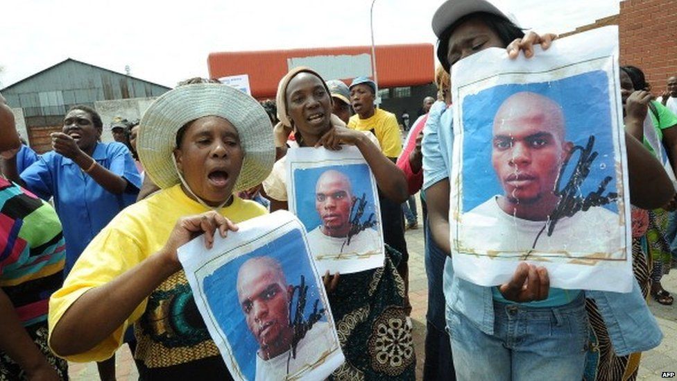 Protesters hold on 8 March 2013 portraits of Mido Macia, a Mozambican taxi driver, outside the Benoni court where police officers charged with murdering him appeared.