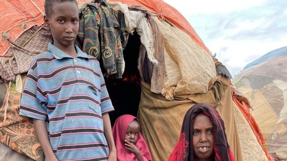 Dahir, a young boy, is seen with his sister and mother in front of a makeshift tent in Baidoa