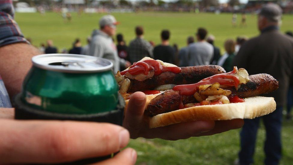 A spectator holds a beer and barbecued sausages at an Australian Rules football match in Melbourne