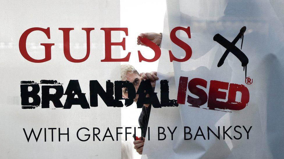 Сотрудник Guess смотрит в окно на Риджент-стрит с надписью «Guess x Brandalised by Banksy»