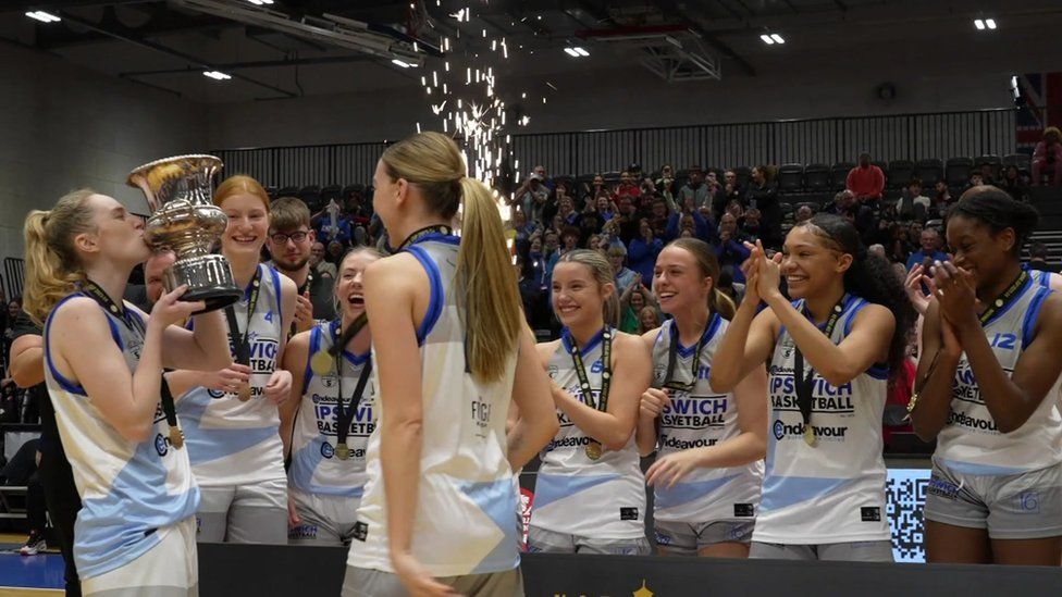 Basketball players lined up and clapping - one is kissing a trophy