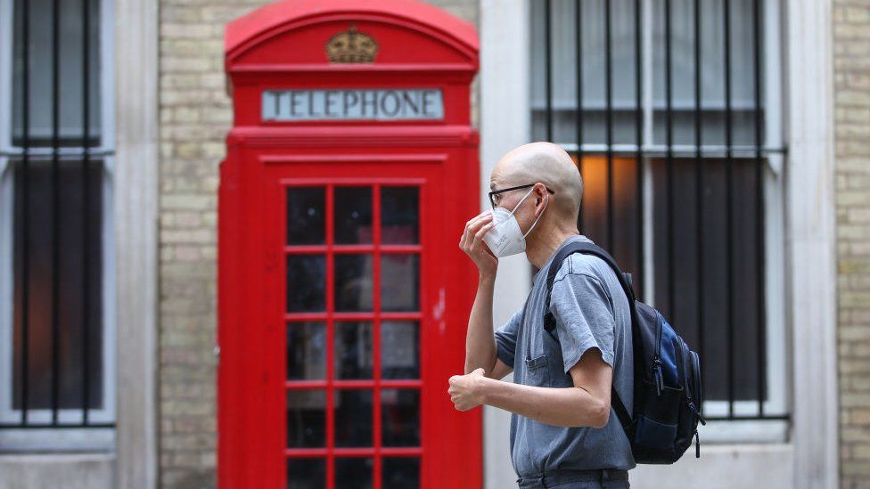 Man walking past phone box in mask