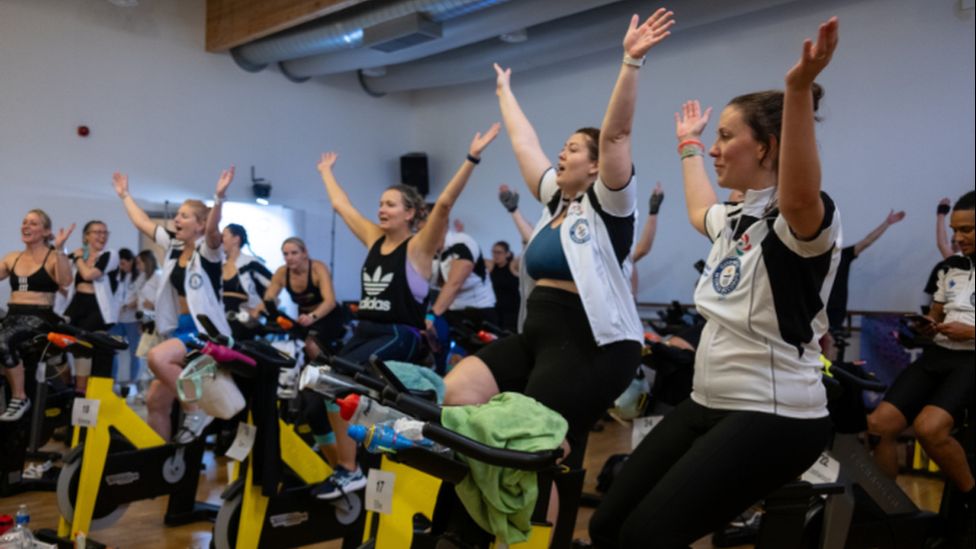 People riding on stationary bikes with their arms raised above their heads