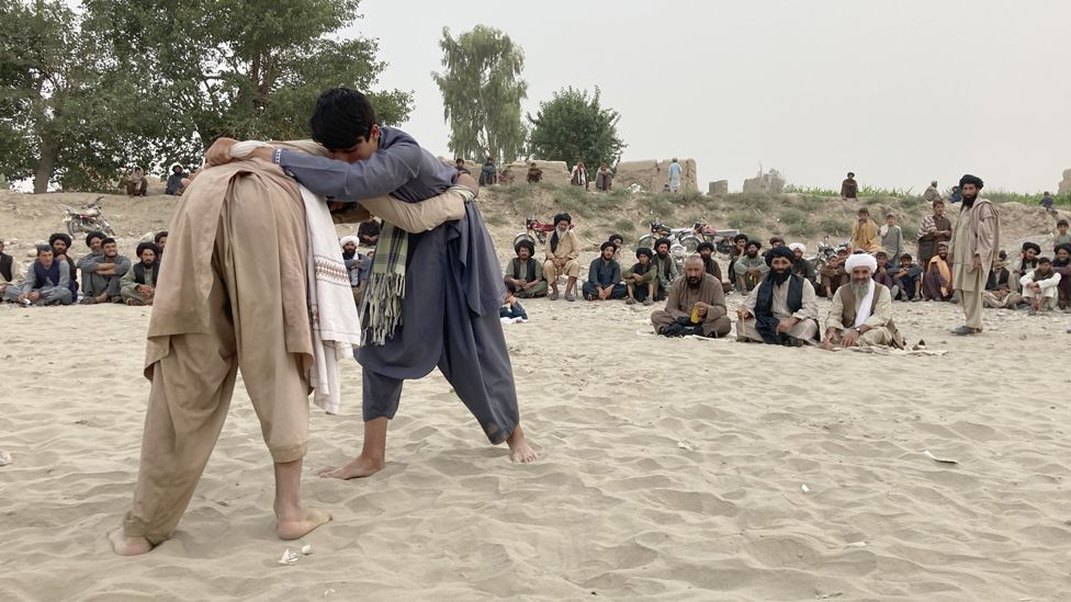 Two young boys wrestling each other as spectators watch