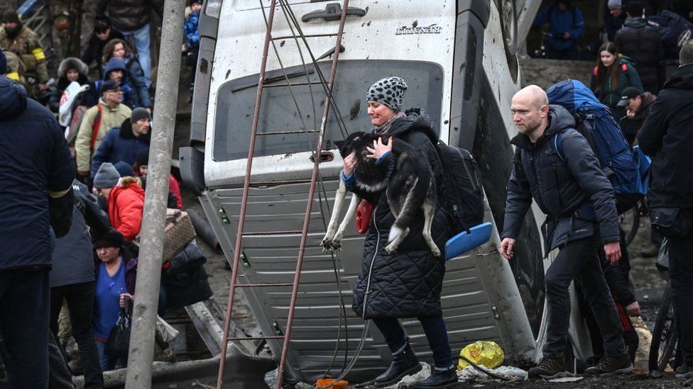 A woman carries a dog while people cross a destroyed bridge in the city of Irpin, northwest of Kyiv, 5 March 2022