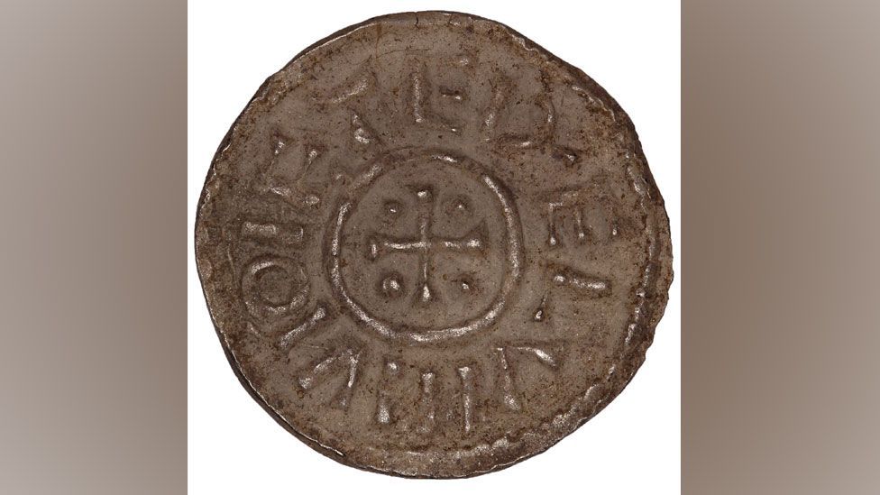 One side of a 9th Century silver coin, on one side showing a Athelstan II's name around the edge and a cross in the middle