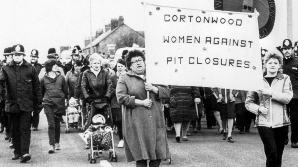 A group of women flanked by uniformed police as they march down the street carrying a banner reading: "Cortonwood women against pit closures"
