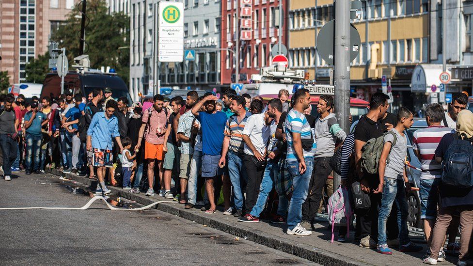 Мигранты стоят в очереди на вокзале Мюнхена, ожидая отправки в центры для беженцев
