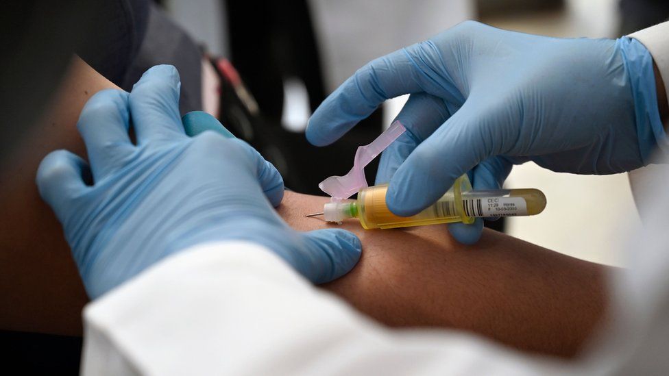 Doctor wearing gloves holds a needle in the arm of a patient