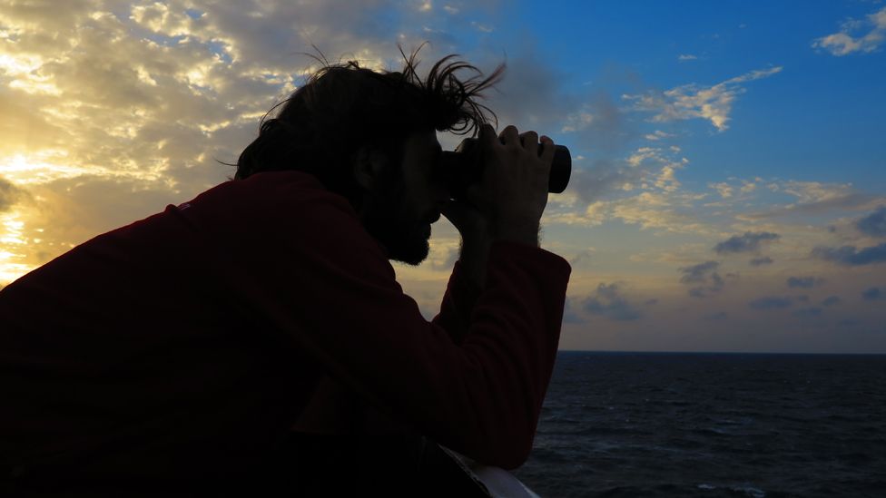 Volunteer looks out to sea through binoculars