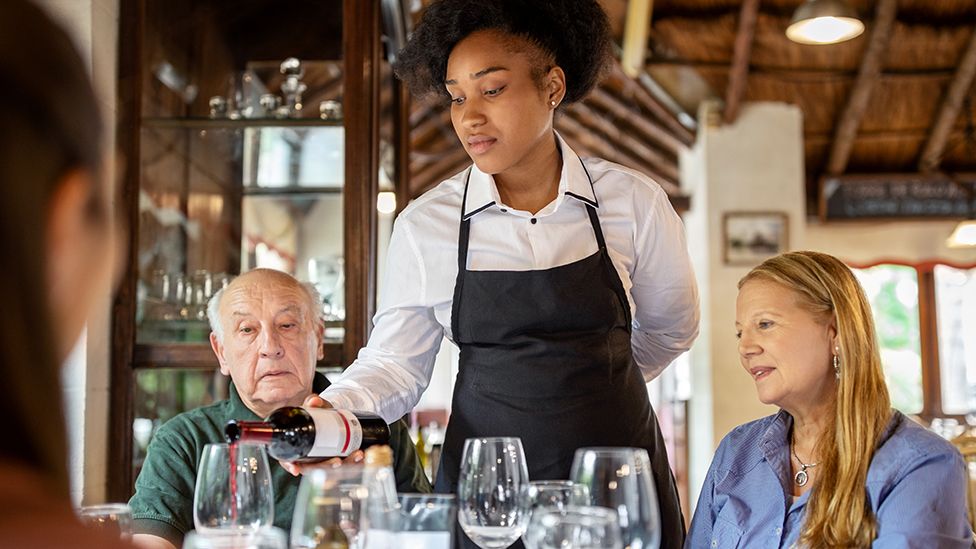 Waitress pouring wine in restaurant with customers looking on
