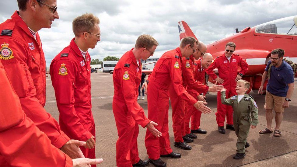 Little boy high-fiving Red Arrows crew on a flight line