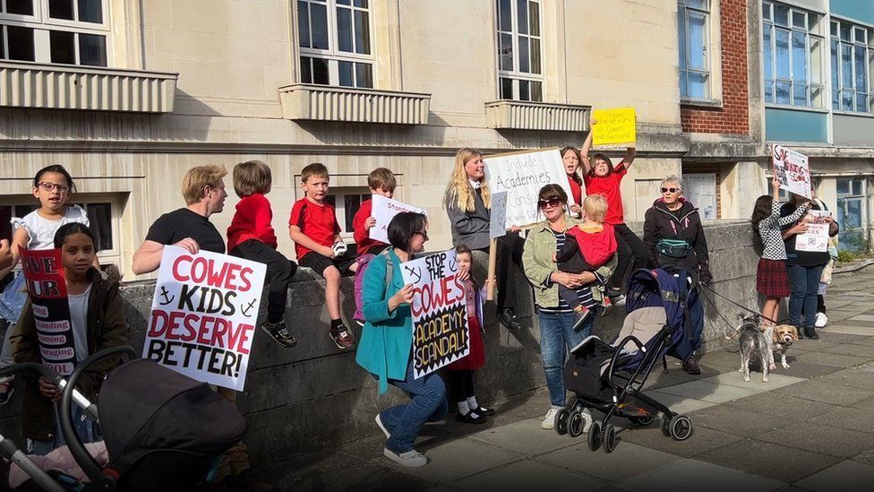 A row of about 15 protesters, children and parents holding placards outside County Hall in Newport