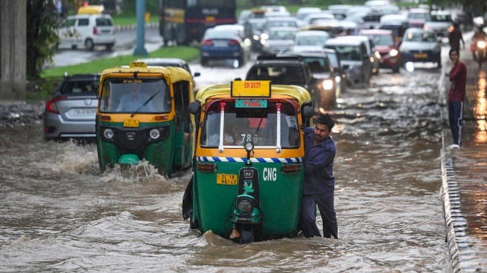Пассажиры едут по сильно заболоченному подземному переходу Бхайрав Марг после муссонных дождей 9 июля 2023 года в Нью-Дели,