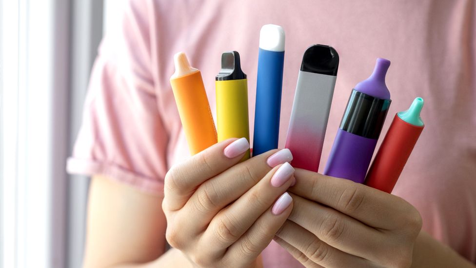 A young person holds a collection of multi-coloured vapes