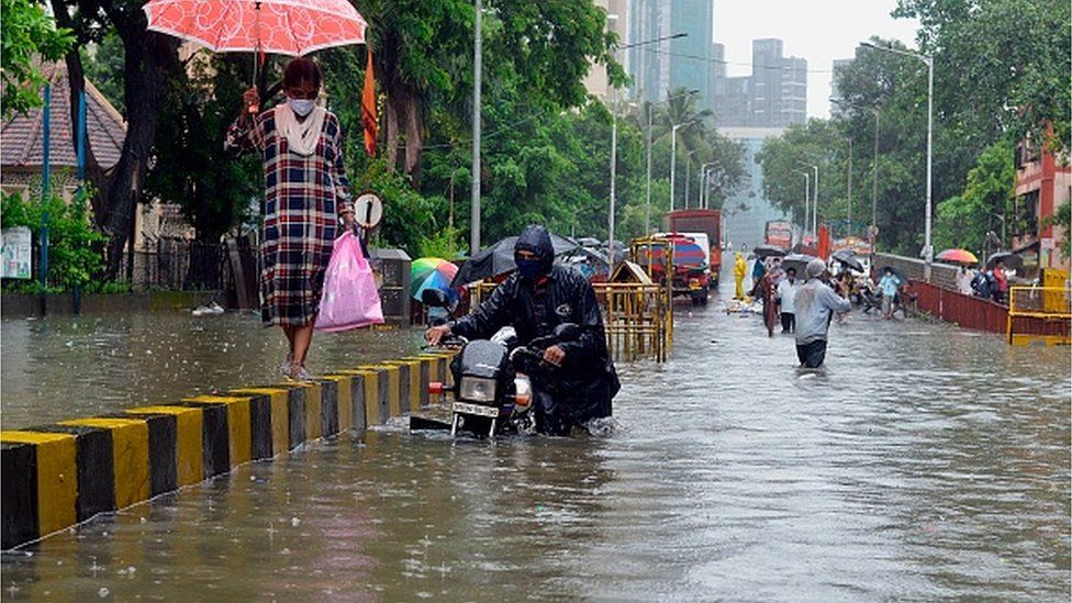 A motorist pushes his stalled bike while a woman walks on a road divider during a heavy monsoon rainfall in Mumbai on August 4, 2020