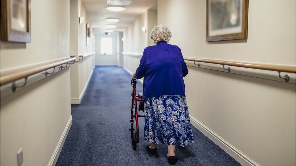 A senior woman walking down a corridor with the assistance of a walker